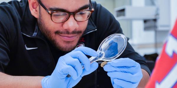 A male student uses a magnifying glass to look at the details of a gold coin